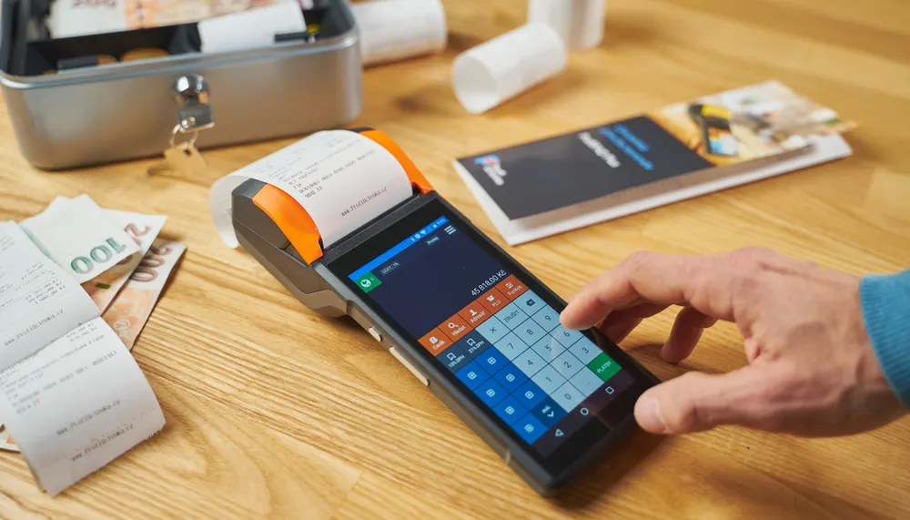 Person reviewing transactions on a payment terminal beside printed receipts.