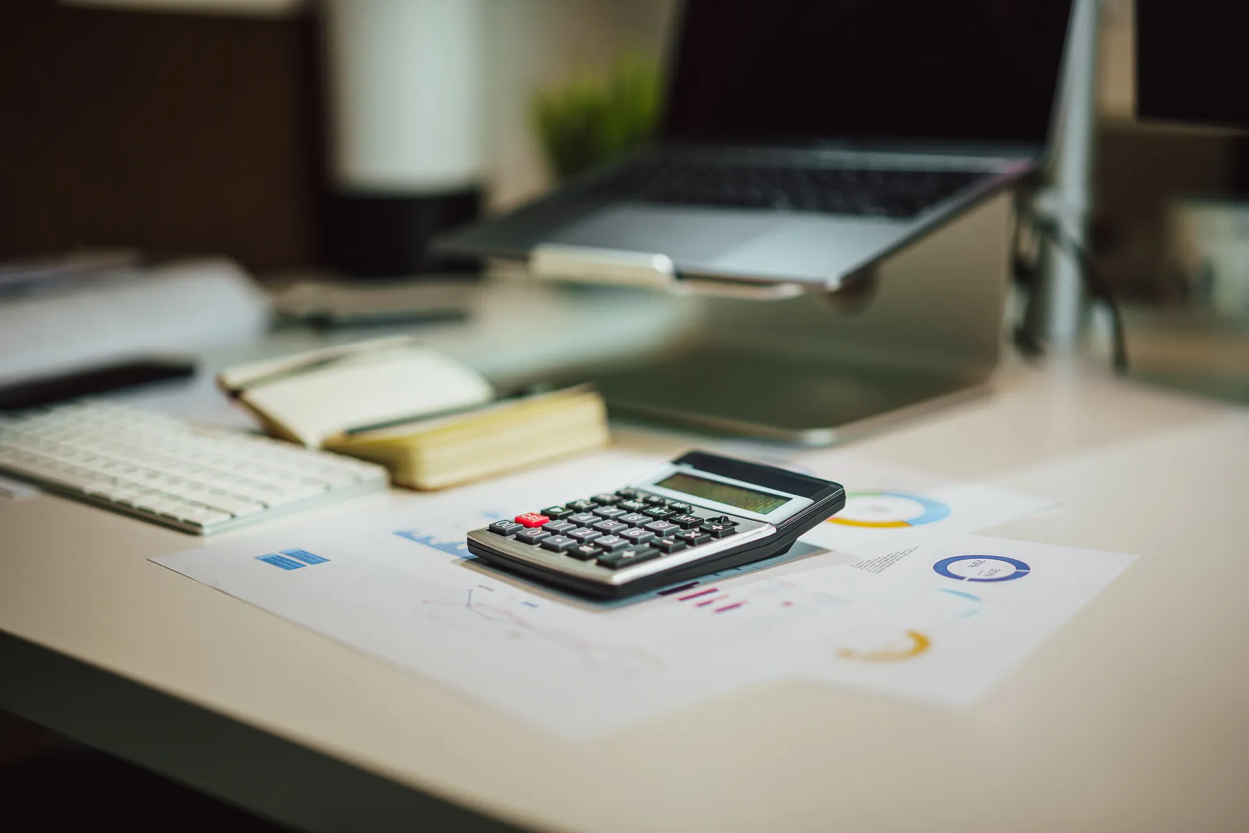 Calculator, laptop, and financial documents arranged on an office desk.